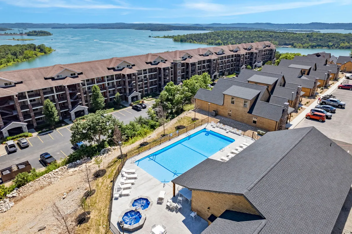A spacious outdoor area featuring a swimming pool, hot tub, and surrounding nature, with apartment-style buildings in the background. The area is lively yet relaxed, offering both water play and spaces for group gatherings or barbecues.