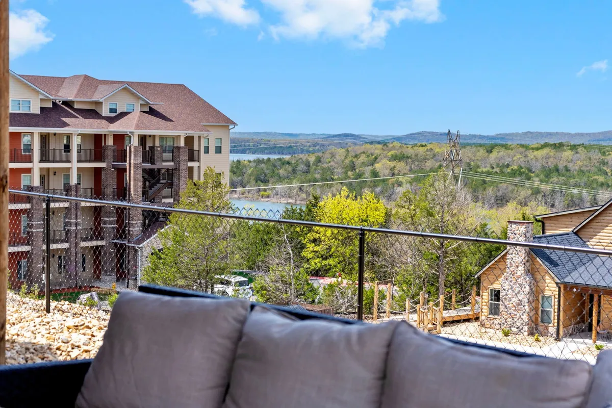 A beautiful view image showing Table Rock Lake, lush green trees, and a multi-story building with a fenced balcony. The scene is tranquil, offering a peaceful spot to relax outdoors while enjoying scenic nature.