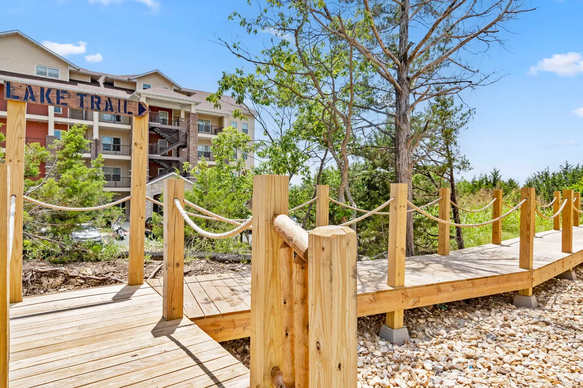 A wooden walkway surrounded by lush greenery leads toward a scenic lake, with the lodge visible in the background. The tranquil setting invites guests to enjoy lakeside strolls and connect with nature.