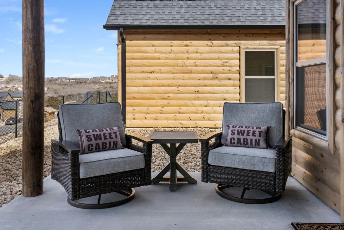 This cozy exterior scene highlights a porch with rocking chairs, a small table, and cabin-themed pillows, all oriented toward enjoying the scenic views. The space is perfect for relaxing with a book, morning coffee, or sharing a glass of wine while immersed in nature.