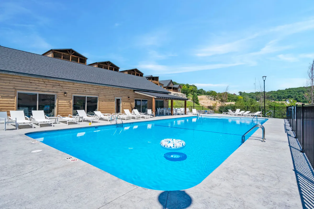 A sparkling outdoor swimming pool surrounded by comfortable lounge chairs, with the lodge building visible in the background. The setting is inviting for both group gatherings and quiet relaxation, capturing the essence of a resort experience.