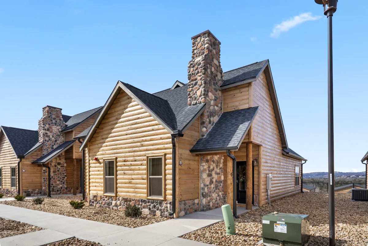 A welcoming log cabin with a classic stone chimney and an inviting front porch set amidst natural surroundings. The porch offers ample space for relaxing and enjoying the outdoors, while the rustic log construction reinforces a cozy, dog-friendly retreat vibe.