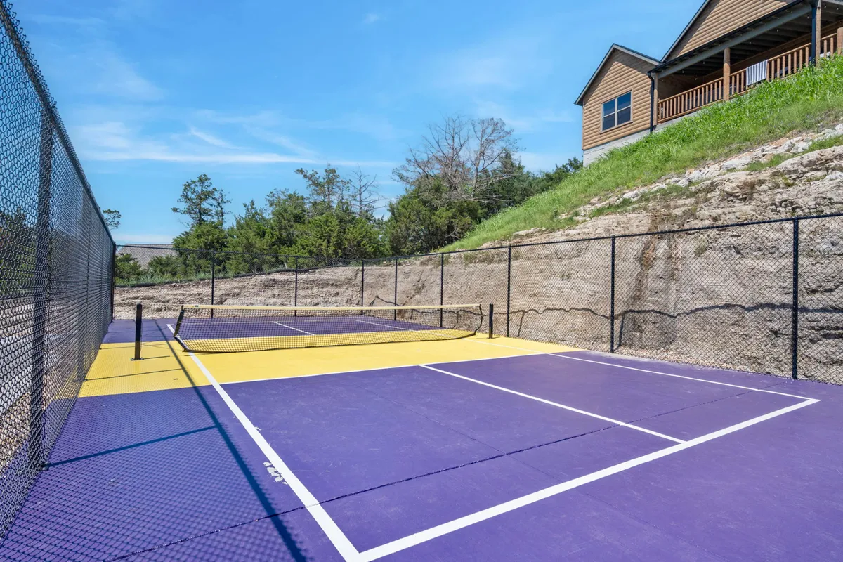 This exterior image features a tennis court surrounded by greenery, with a house in the background. The scene feels energetic yet relaxed, evoking community and outdoor activity.