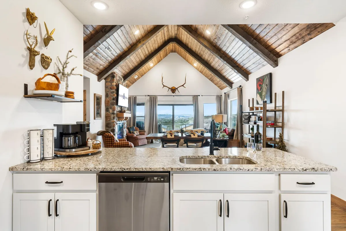A view encompassing the granite kitchen countertop, a cozy seating area, a stone fireplace, and expansive windows with a view. The mix of kitchen, lounge, and fireplace creates a holistic sense of the open-concept layout and shared experiences.