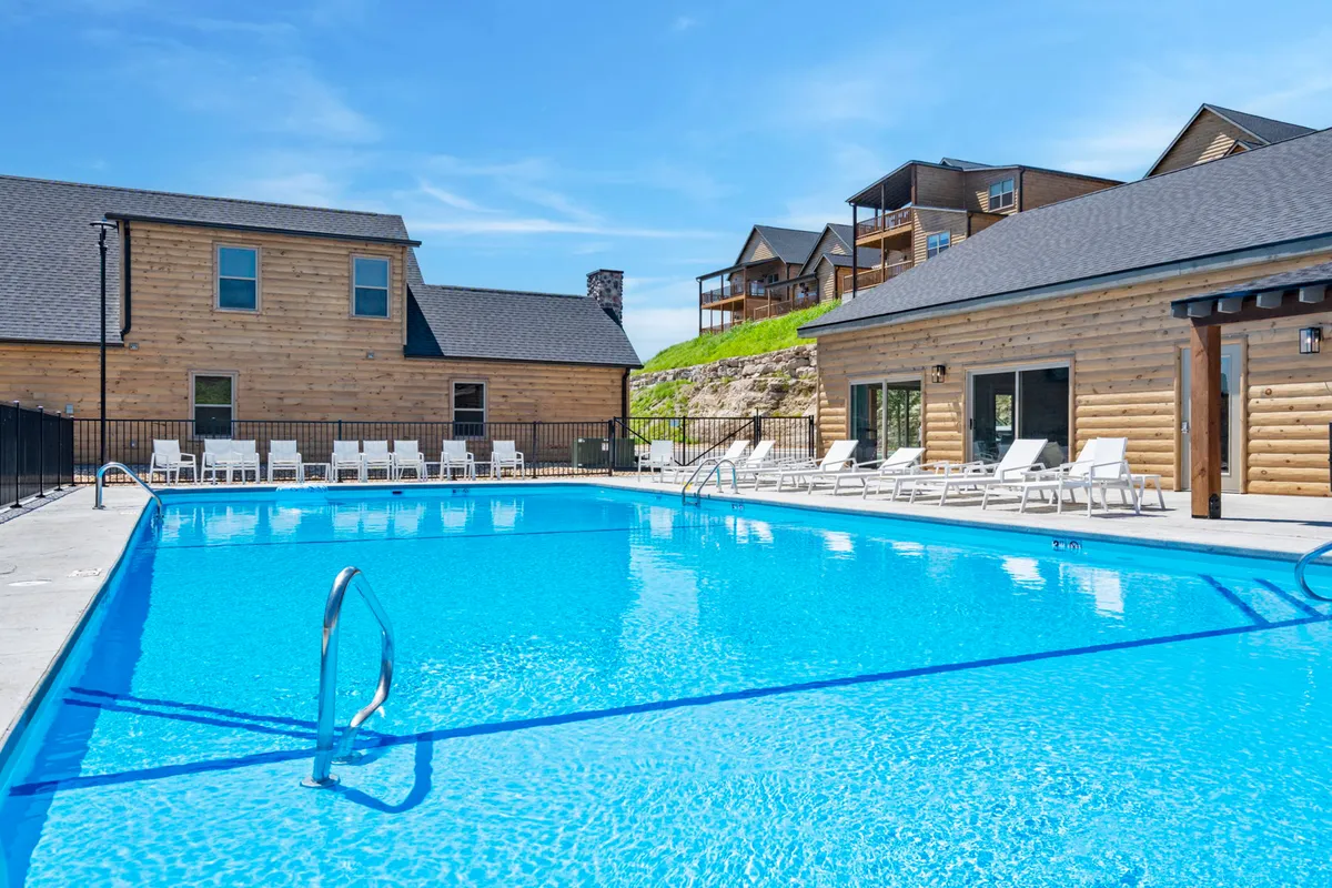An inviting outdoor swimming pool is surrounded by wooden cabins and lounge chairs, inviting guests to swim, sunbathe, or relax. The mood is leisurely and refreshing, ideal for both recreation and relaxation.