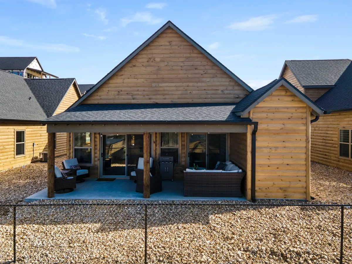 An exterior shot of a wooden cabin’s covered porch, complete with comfortable outdoor seating and a grill. The setting looks out over scenic nature, ideal for enjoying meals outside or unwinding with a drink while taking in the tranquil surrounds.