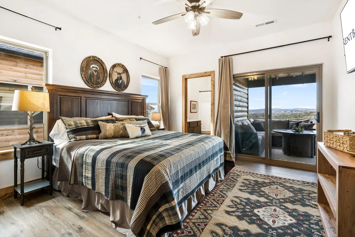 A serene king bedroom with a comfortable bed, sliding glass doors opening to a patio, and decorative wall plates. The natural light streaming in and the view to the outdoors invite guests to start their day with fresh air and beautiful scenery.